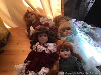 Photo of five collector dolls on a wooden surface with curtain background showing their clothing and hairstyles.