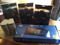 Photo showing two white desktop speakers, three new sealed NHL headset packages, and boxed Adesso EasyTouch 130 keyboard.