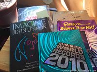 Five hardcover books stacked partly overlapping, titles visible include Imagine John Lennon, Ripley's Believe It or Not, Guinness World Records 2010, How Things Come Apart, Star Wars Technical Journal.