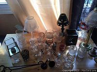 Overview of assorted glass and candle holders displayed on table including the brass lamp-style candle holder with glass shade and iron snuffers.