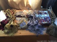 Wide view of an assortment of drapery tiebacks laid on wooden surface, showing various colors and sizes including gold, maroon, purple, and lavender cords with tassels.