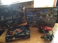 Mega Bloks X-Trek II, Block Bots, and Street Rod sets in their original boxes on table with two assembled toy figures nearby.