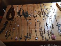 Full view of all necklaces arranged on wood table featuring varied styles and materials including metal, glass beads, and ceramic elements.