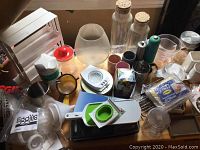 Photo showing various kitchen utensils and containers including glass canisters, ceramic cups, juicer, and others spread on a surface.