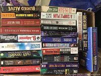 Photo showing more paperback books in stacks with titles such as Stay Close by Harlan Coben, Saving Rachel by David Baldacci, and other suspense and thriller novels.