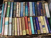 Photo of the lot showing multiple paperback and hardcover books stacked closely in a box. Visible authors include Nora Roberts, Danielle Steele, Belva Plain, and more.
