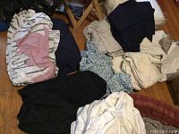 Photo showing a mix of folded bedding linens in multiple colors, including a floral patterned duvet cover, solid colored sheets in dark and beige tones.