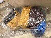 Five knit crocheted afghans of various colors and sizes wrapped in plastic bag.