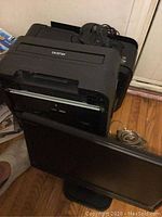 Brother HL22 black laser printer viewed from front with paper tray visible, placed on wooden floor next to wall