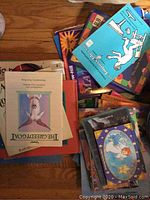 Box of assorted children's books lying on floor with visible titles like The Barefoot Book and other colorful covers