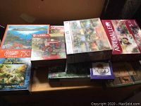 Photo showing multiple puzzle boxes stacked together on a surface. Includes various brands and themes, highlighting range of sizes and designs.