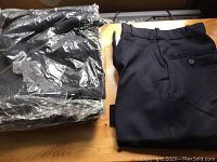 Seven pairs of navy blue ladies work pants, folded and one still partially in packaging, neatly stacked on a surface.