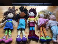Five dolls arranged side by side on a wooden table: four rag dolls and one Ty Beanie Baby bull doll.