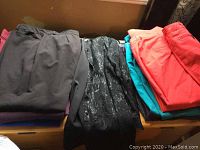 Photo showing folded assortment of women's pants in various colors including black, dark gray, coral and turquoise.