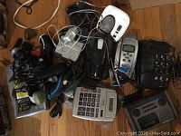 Photo shows a collection of various phones, two electric razors, a basic calculator, and related cables on a wooden surface.