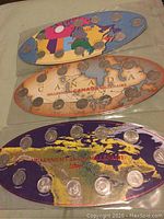 Three oval-shaped plaques for coin collections laid flat, showing Canadian maps and attached provincial quarters from 1992, 1999, and 2000 collections.
