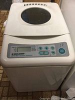 Top view of Black & Decker bread maker showing control panel with buttons and start/reset button, and viewing window on lid.