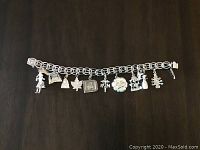 Sterling silver charm bracelet laid flat displaying all 9 attached charms in a row on a dark surface.