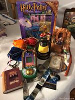 Collection of Harry Potter toys and collectibles including a handheld electronic game, card deck in tin, sticker set, and lanyard displayed on a table.