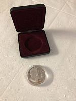 Photo showing the 1995 Canadian silver coin with the portrait of Queen Elizabeth II, next to a red velvet-lined black display case from front angle.