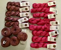 Overhead shot showing all 18 skeins arranged flat: 8 copper-colored wound cakes on the left and 10 fuchsia twisted skeins on the right.