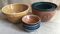 Three nested Monty’s terracotta mixing bowls with green glazed interiors and one larger cream-colored mixing bowl with embossed design shown side by side.