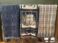 Three cotton blankets hanging over a wooden railing, showing their patterns and fringed edges