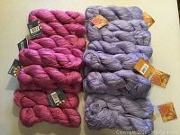 21 skeins of yarn, 11 mauve and 10 pink, arranged in two groups with labels visible