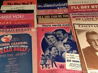 Image shows a close-up of various vintage sheet music items including 'Hello Dolly', 'You'll Never Know', and others with illustrated covers and vintage typography.