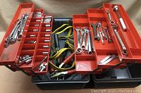 Opened red plastic toolbox showing sockets, ratchet, and jumper cables inside.