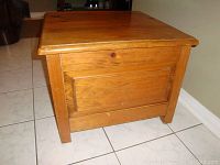 Front and side view of square pine wooden storage box or coffee table with panel design and natural finish, showing slight wear and wood knots.