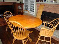 View of the solid oak round dining table with pedestal base and four matching oak chairs surrounding it, displayed indoors on hardwood floor near fireplace.