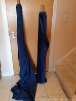 Two rolls of blue fabric standing against a door and wall, showing length and drape.