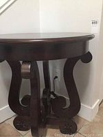 Side view of the dark wooden circular side table showing the scroll-shaped legs and sturdy cross base.