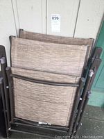 Two folded lawn chairs stacked showing brown metal frames and tan woven fabric