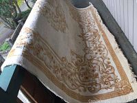 Carpet partially rolled showing beige and brown ornate floral design with frayed edges and worn areas.