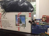 Box labeled Pin Concorde Christmas Tree 6.5 foot with 280 LED lights, taped with Canadian flag tape, with black garbage bag on top.