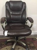 Front view of brown leather office chair, showing padded backrest, armrests and base with wheels.