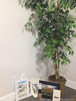 Artificial tree standing in corner by wall socket with several small artwork pieces leaning at base
