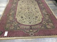 Full view of carpet showing beige center area with floral and scroll motifs in purple and green, bordered by mauve with additional scroll design and beige edging.