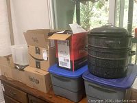 Boxes and bins stacked on table with large black speckled enamel canner pot on top.