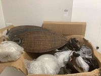 Two sets of wicker-style fan blades and unassembled ceiling fan parts in a box with bubble wrap.
