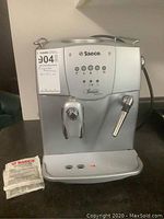Front view of silver Saeco Incanto machine alongside unopened Saeco cleaning tablets pack