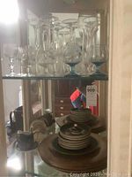Glassware including wine and aperitif glasses on glass shelving, with copper and ceramic serveware below