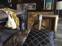 Wide view showing stool with leopard print upholstery, cushions, and framed large animal artwork in background