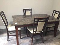 Full view of the dining table with all four chairs around it, showing the marble-patterned top and beige cushions on chairs.