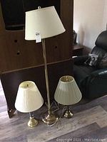 Full view of floor lamp and two table lamps, showing brass bases and white lampshades.