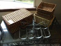 Woven picnic basket, metal wine rack, and two smaller woven baskets displayed on glass table.