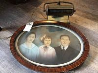 Oval wooden picture frame with beaded trim containing hand-colored vintage family portrait of three people
