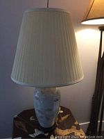 Full view of the ceramic table lamp showing the pleated beige lampshade and the ceramic base with leaf motif.